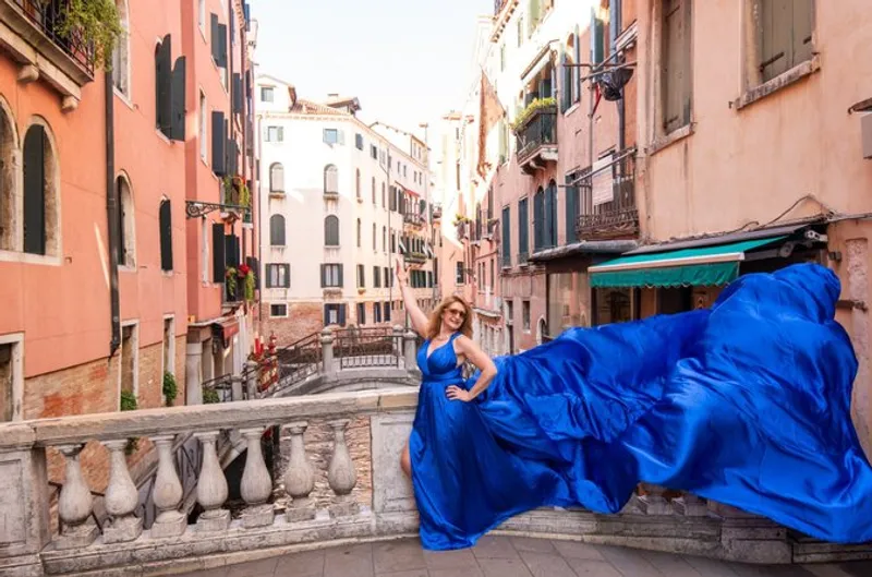 Woman in a blue flying dress on a stone bridge during a venice flying dress photoshoot between terracotta facades