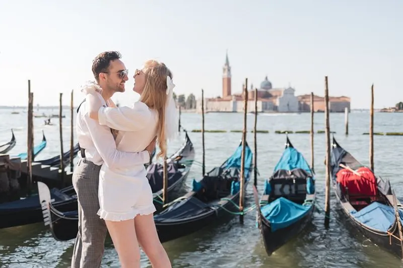 Bride and groom embracing by moored gondolas during a venice wedding photoshoot with San Giorgio across the water