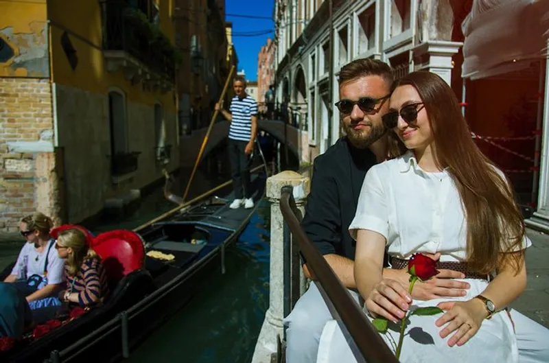 Couple with a rose beside a narrow canal during a venice proposal photoshoot with a gondola passing behind